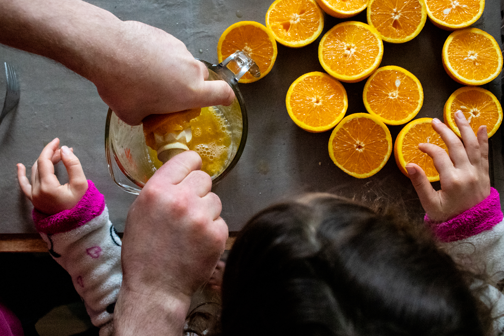 Père montrant à sa fille à presser des oranges, vue du dessus, on ne voit que les mains